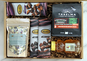 Display of items that can make up a Gratitude Box, including three bars of Bedré chocolate, one bag of Sakari Farms tea, one bag of Takelma Roasting Co ground coffee and one adorable bear-shaped honey bottle.