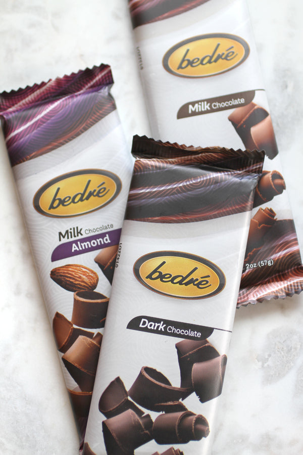 Three wrapped chocolate bars (milk, dark and milk with almonds) are laying flat on a marble background.