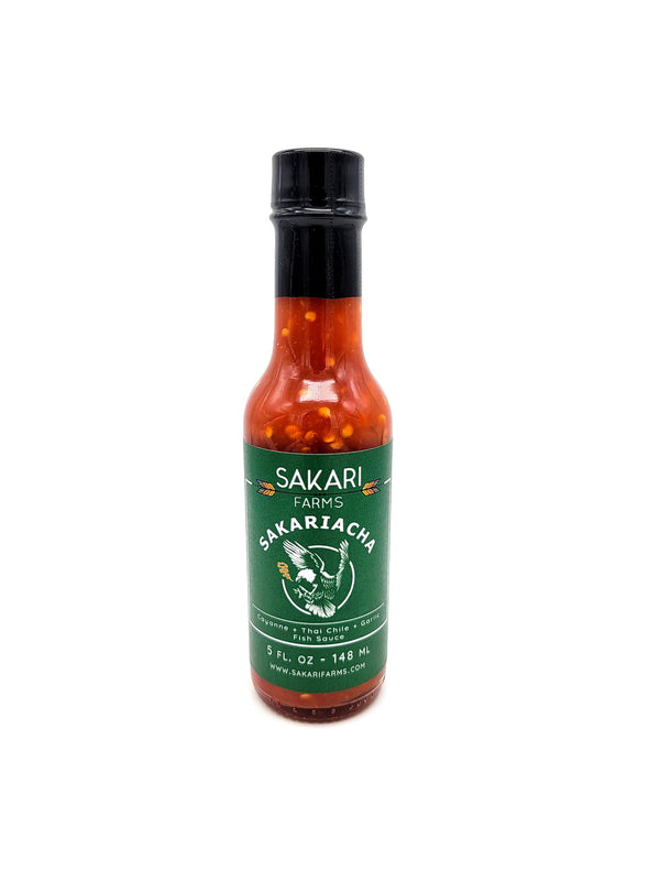 A 5oz bottle of dark orange hot sauce with pepper seeds on a white background. The label reads SAKARI FARMS SAKARIACHA HOT SAUCE.