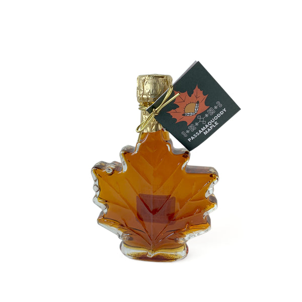 Small maple shaped glass bottle filled with amber colored maple syrup from Passamaquoddy Maple on a white background.