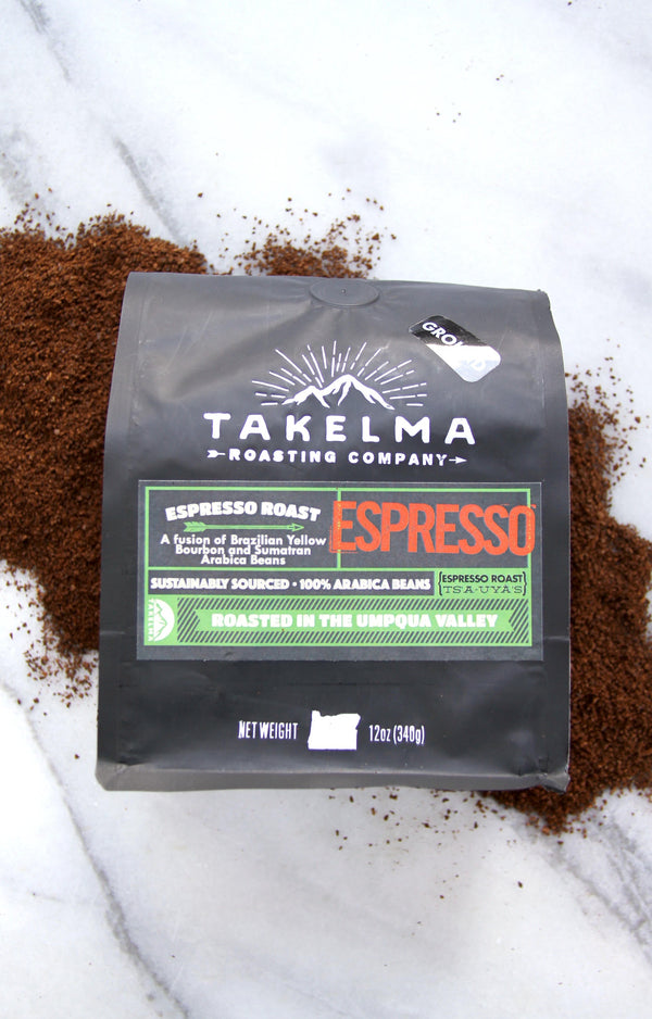 A bag of Espresso ground coffee from Takelma Roasting Co sitting on a pile of ground espresso with a marble background.