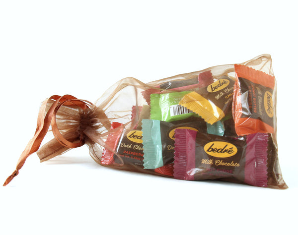A gauze bag with an assortment of 12 individually wrapped chocolate Meltaways from Bedré chocolatier, all on a white background.